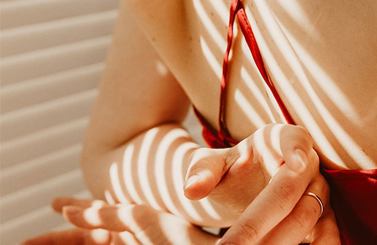 Frau mit rotem Top, die ihre Hände in Sonnenlicht mit Streifeneffekten hält, symbolisiert Hautpflege und Sonnenschutz.
