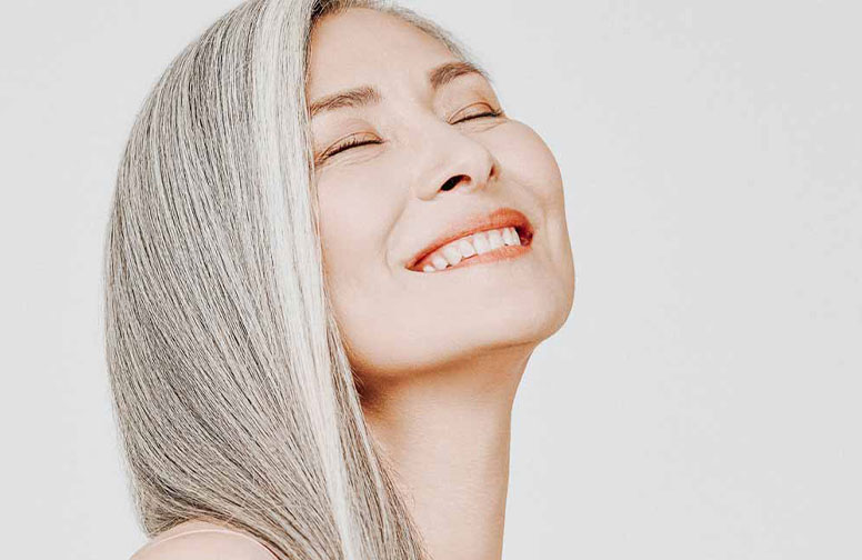 anti-aging-geheimniss-02 Lächelnde Frau mit grauen Haaren und strahlender Haut, repräsentiert die Anti-Aging-Vorteile von Hautpflegeprodukten mit weißem Tee.