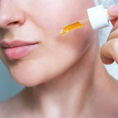 Frau trägt Vitamin-C-Serum mit Pipette auf ihre Haut auf, demonstriert Anwendung für strahlende Hautpflege.