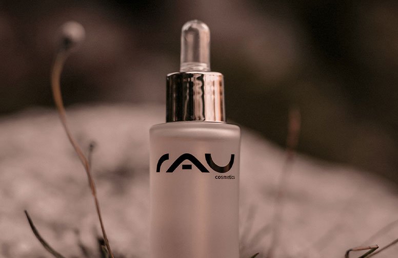 Flasche mit Gesichtsöl von RAU Cosmetics, transparentes Design, Pipette, im natürlichen Umfeld, passend zu entspannender Hautpflege-Routine.